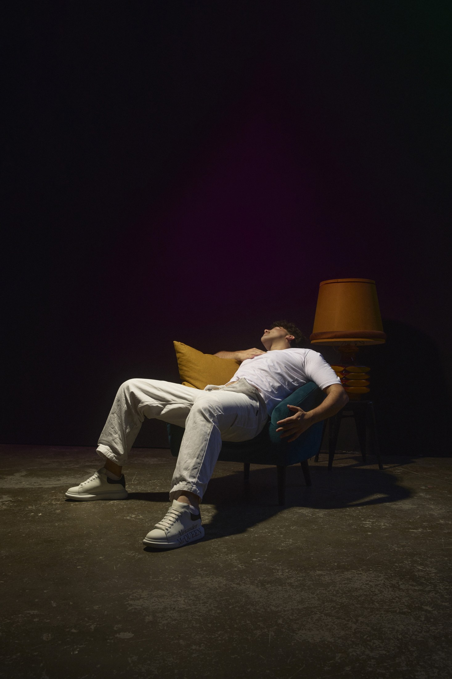 Adam reclining in a teal chair beside an amber lamp